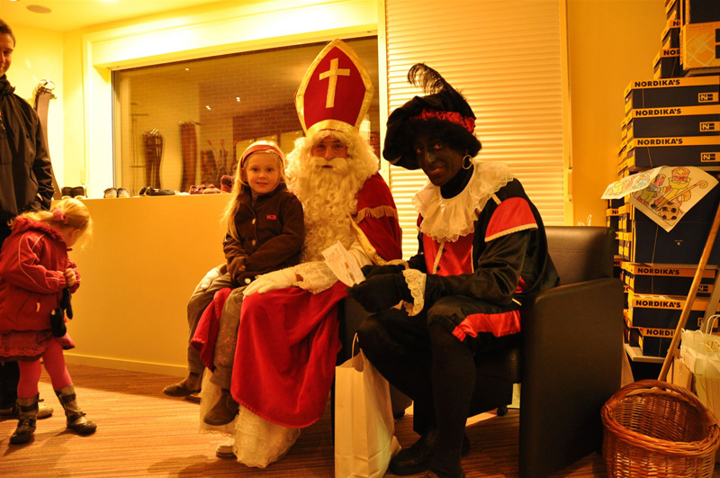 Zwarte Piet en Sinterklaas met een meisje op schoot